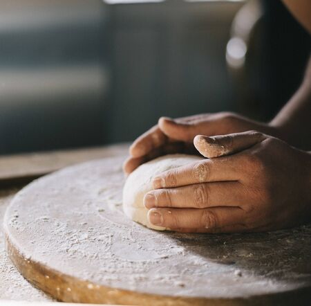 Man kneading and baking homemade pizza dough in the kitchen. Closeup on baker's hands preparing loaf...