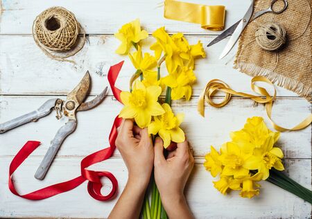 Top view of florist hands making flower bouquet with narcissus and decorative ribbon. Vintage flower shop and bouquet making in springtime.の写真素材
