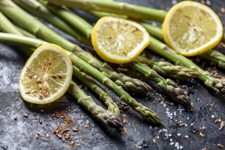 Fresh asparagus dish with lemon and spices on black plate closeup. Vegetarian cuisine recipe.の写真素材
