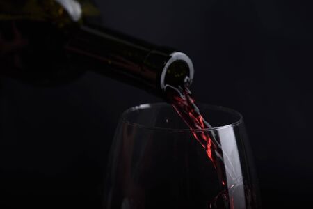 Red wine pouring in wine glass over black background. Closeup of red wine splashing in wineglass in restaurant. Wine tasting.の写真素材