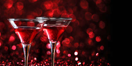 Two martini glasses in front of red bokeh background. Luxury cocktail drink in restaurant bar with night lights blur. Classy beverage celebration party for new year, christmas, valentine and anniversary event.の写真素材