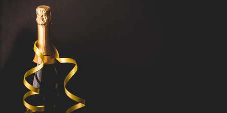 Luxury new year background. Christmas celebration panoramic design banner. Champagne bottle with gold ribbon on dark background.の写真素材