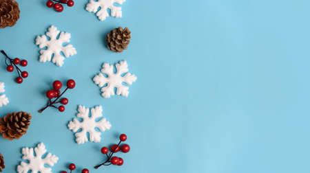 Minimal christmas, new year and winter holiday composition. Flat lay. Creative banner with snow flakes, red berry and pine cone on pastel blue background. Christmas and wintertime concept. Top view.の写真素材