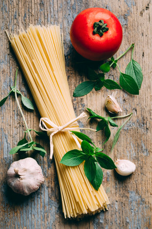 Italian pasta food ingredients on rustic wooden table from above. Top view of spaghetti, garlic, tomato and basil for bolognese sauce recipe. Mediterranean cuisine restaurant menu.の写真素材