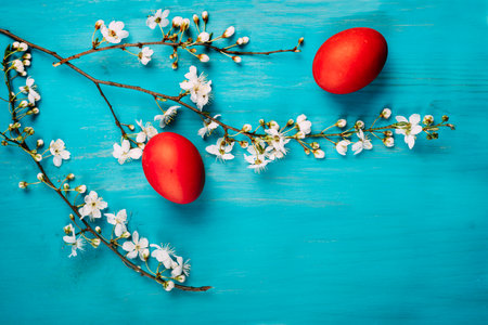 Red easter eggs and spring flower blossom decor on grunge wooden table from above. Colorful bright easter holiday greeting card. Top view of traditional painted easter eggs on vintage blue background. Still life flat lay.の写真素材