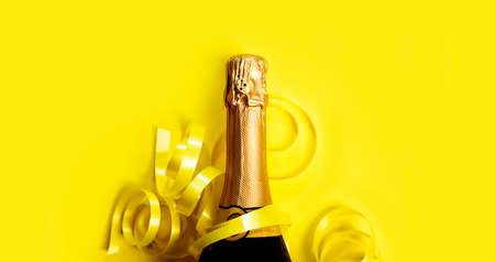Champagne bottle with gold ribbon on pastel yellow background. New year celebration banner design. Minimal flat lay christmas celebration border.の写真素材