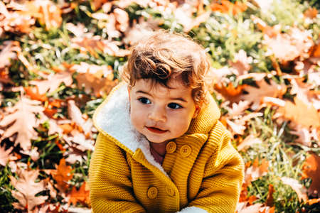 Happy little girl in yellow jacket playing with autumn leaves in park. Child smiling and having fun in forest.の写真素材