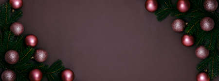 Shiny pink christmas baubles and fir tree frame on dark brown background. Elegant new year flat lay greeting card design with holiday design.の写真素材