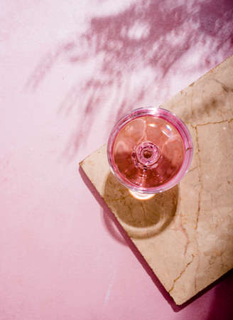 Pink champagne in glass on luxury marble table with palm shadow. Summer beach cocktail party with  rose wine alcohol beverage on textured background with tropical plant shade. Top view.の写真素材