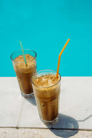 Summer holiday vacation with frappe refreshment by luxury poolside. Two ice coffee cups with straws...