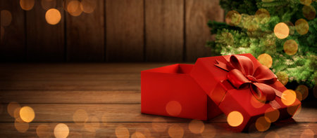 Red christmas present tied with ribbon under christmas tree with lights. Cozy magic xmas and new year holiday scene. Open gift box on rustic wooden background with copyspace.の写真素材
