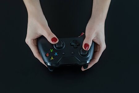 Top view of woman hands with red nail polish on fingers holding a logo free modern gaming controller for playing digital video games isolated on black for fun  leisure entertainmentの写真素材