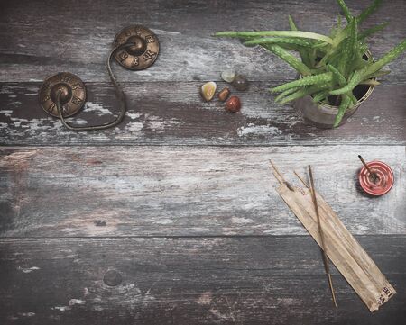 Rustic wooden table for text copy,  with green aloe vera plant, burning incense, incense sticks, small rounded energy healing stones in earthy colors and Tibetan meditation prayer bells with the spiritual words Om mani padme hum, commonly translated as The jewel is in the lotus. .の写真素材