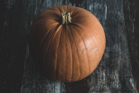A big dark and moody traditional orange pumpkin on rustic vintage wood floor as concept of halloween...