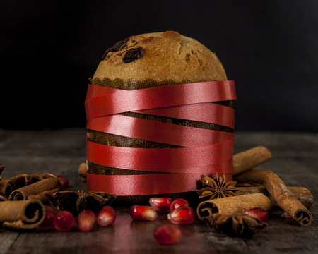 An Italian panettone with cinnamon, star anise, and pomegranate beans on a wooden background in front of a black backgroundの写真素材