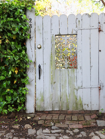 A rustic wooden gate with a decorative iron insert. Ivy and cobblestones accent the scene.の写真素材