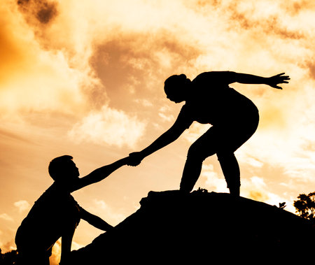 silhouate of woman and man holding hand in hand on different levil of the rockの写真素材