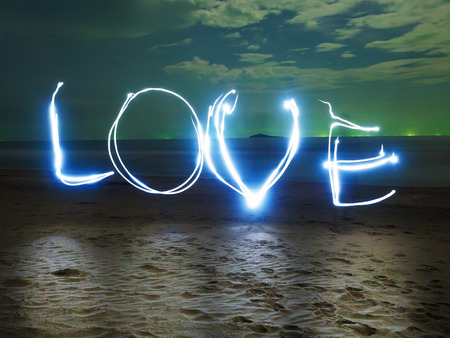 hand writing the word of LOVE, by using flash light, on the night at sea beach