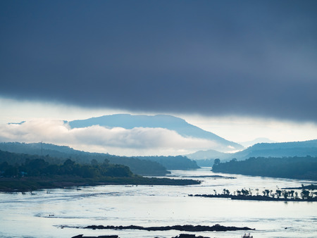 silhouette of the trees in land and mountain breaking by big river, on the morning lightの写真素材