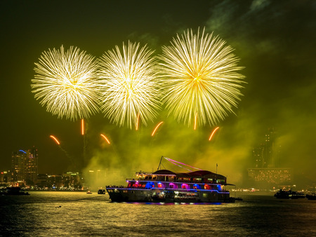 Colorful holiday fireworks in the night sky with boat floating on the sea and the city in backgroundの写真素材