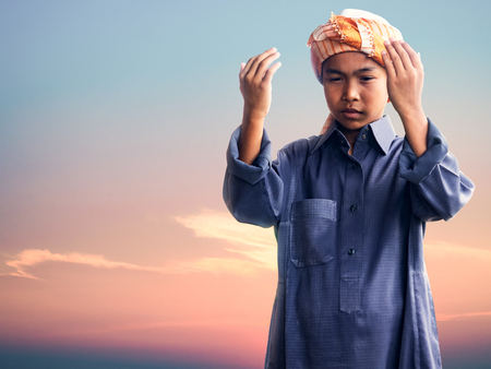muslim child praying for Allah, muslim God, on the sunset sky backgroundの写真素材