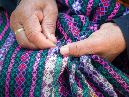 old woman's hand sewing on crafting cloth, traditional homemade fabric with needle and threadの写真素材