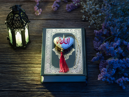 Quran or Kuran, the islamic holy book, in dark wooden background with lantern and rosary with arabic text "Allah"の写真素材