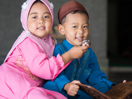 happy muslim girl with full hijab in pink dress , asian traditional style dress playing stethoscope with her brother inside mosque.の写真素材