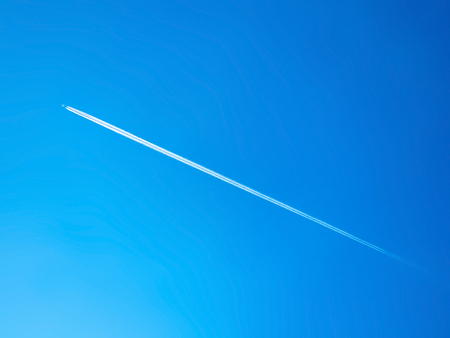 long contrail cloud of smoke from jet engine of the airplane over the blue skyの写真素材
