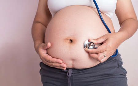 pregnant woman applying ears stethoscope on her belly to observe her baby. Maternity or motherhood concept.の写真素材