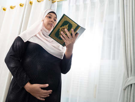 pregnant muslim woman with full traditional dress reading the Quran holy book  of all muslim . Maternity  or motherhood concept.の写真素材