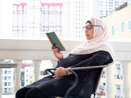 pregnant muslim woman with full traditional dress reading the Quran holy book  of all muslim . Maternity  or motherhood concept.の写真素材