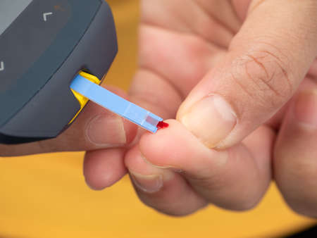 Close up shot of woman's hands making blood sugar level test by Glucose meter using as indicator of...