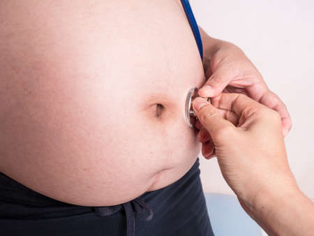 pregnant woman applying ears stethoscope on her belly to observe her baby. Maternity or motherhood concept.の写真素材