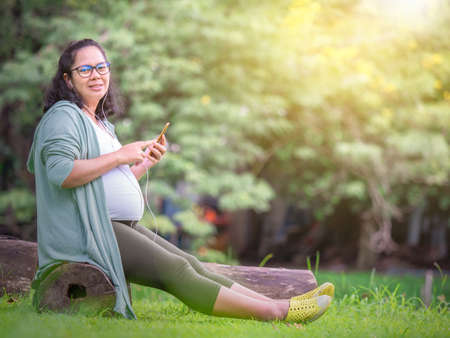 Pregnant women sitting in the park and relaxing under the tree by pregnancy related positionの写真素材