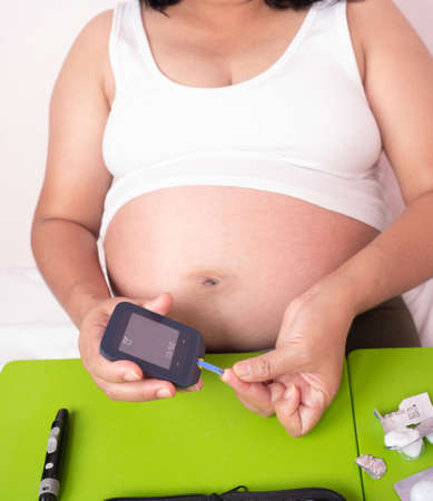 Close up shot of pregnant woman's hands making blood sugar level test by Glucose meter using as indicator of diabetes, and for pregnancy awareness of glycemia, health care concept.の写真素材