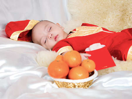 cute asian four-month baby in chinese traditional red dress sleeping with orange: symbol of lucky  gift  in chinese newyear festival. Happy chinese new year concept.の写真素材