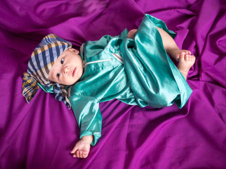cute asian four-month baby in islamic traditional dress sitting on chair  with the hat style of...
