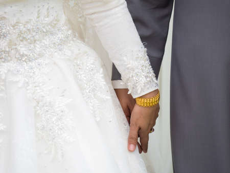 closeup shot of hands of bride and groom with wedding rings and bouquet in celebrating eventの写真素材