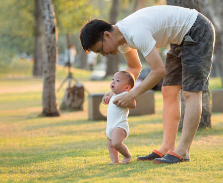 cute asian six-month baby in white dress smiling with his father in garden.の写真素材