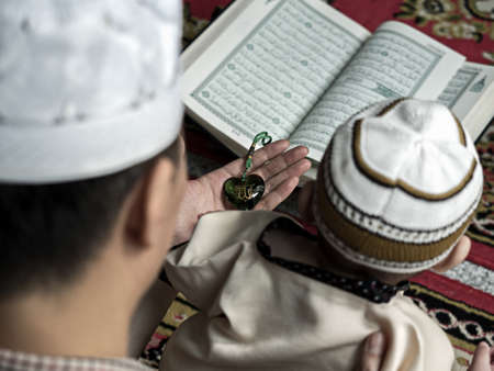 cute asian six-month baby in traditional muslim style dress preying with his father in ramadan festival. ramadan concept.の写真素材