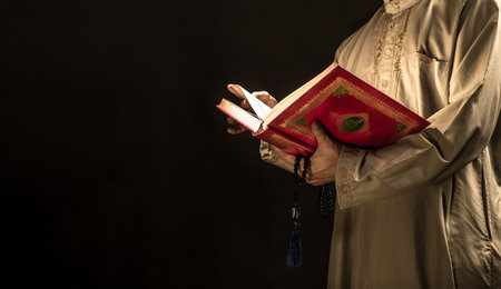 Man reading the Quran or Kuran ( the islamic holy book) on black background with rosary bead in ramadan night, muslim style and ramadan conceptの写真素材