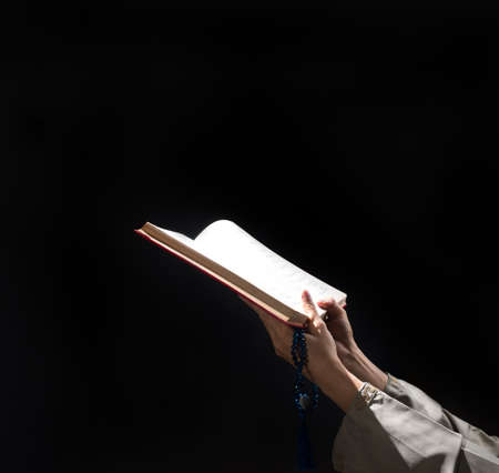 A man with his hand hold the Quran or Kuran ( the islamic holy book) on black background with rosary bead in ramadan night, muslim style and ramadan conceptの写真素材