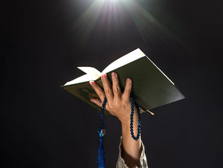 A man with his hand hold the Quran or Kuran ( the islamic holy book) on black background with rosary bead in ramadan night, muslim style and ramadan conceptの写真素材