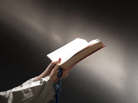 A man with his hand hold the Quran or Kuran ( the islamic holy book) on black background with rosary bead in ramadan night, muslim style and ramadan conceptの写真素材
