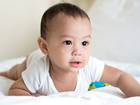 cute Asian male baby in white dress smiling with his mother in bedroom at home