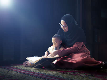 happy asian little child studying on his Kuran book with his mother at home in ramadan month of Islam, study and education conceptの写真素材