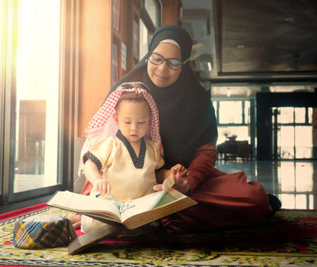 happy asian little child studying on his Kuran book with his mother at home in ramadan month of Islam, study and education conceptの写真素材