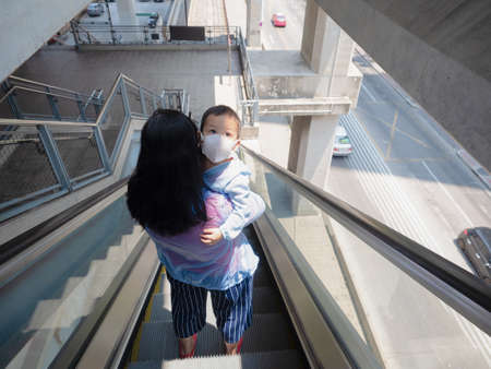 Asian child and his mother wearing white face mask to prevent Coronavirus,which official name for...