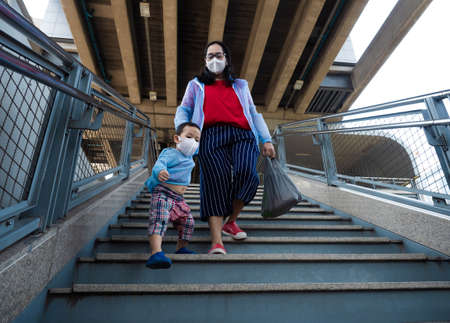 Asian child and his mother wearing white face mask to prevent Coronavirus,which official name for...